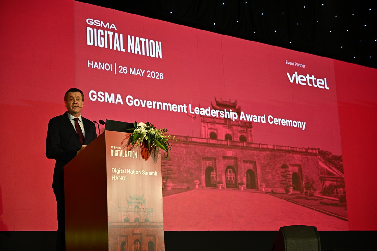 Người đàn ông vest đen, cà vạt đỏ phát biểu tại sự kiện GSMA với màn hình đỏ và logo Viettel.