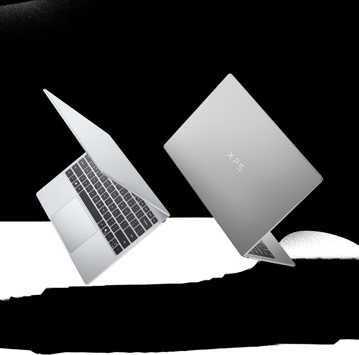 Hai chiếc laptop Dell XPS màu bạc trên nền đen, một chiếc mở màn hình sáng xanh.